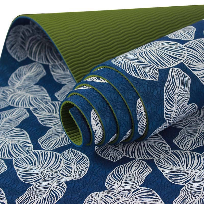A rolled-up yoga mat with a blue surface featuring a white leaf pattern and a textured green underside—ideal as custom merchandise or unique promotional products.
