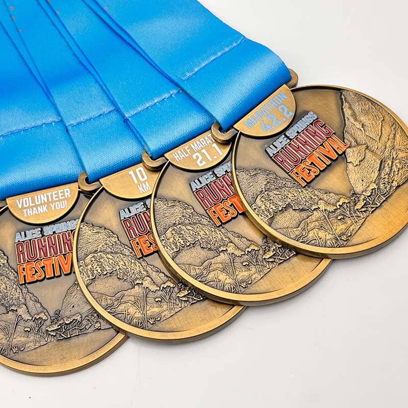 Five bronze-colored medals with blue ribbons are displayed as custom merchandise. Each medal, ideal as promotional products, reads "Running Festival" and features categories: Volunteer, 10K, Half Marathon 21.1, and Marathon 42.2 km.